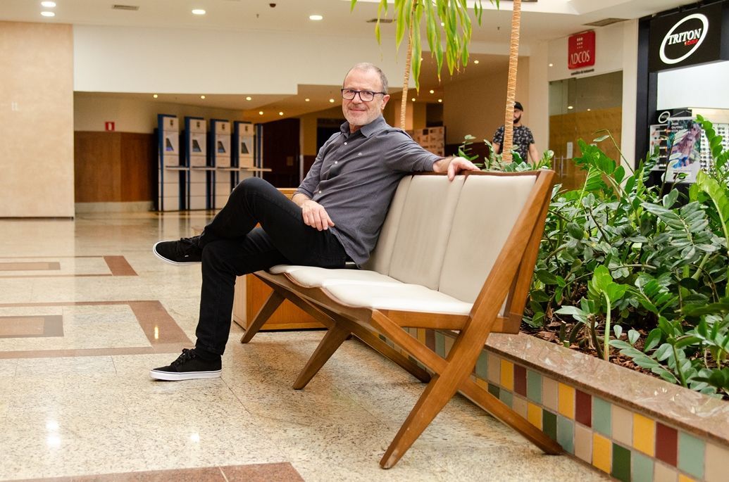 Um homem está sentado em um banco de madeira em um shopping.