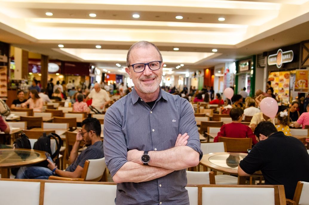 Um homem está em uma praça de alimentação com os braços cruzados.
