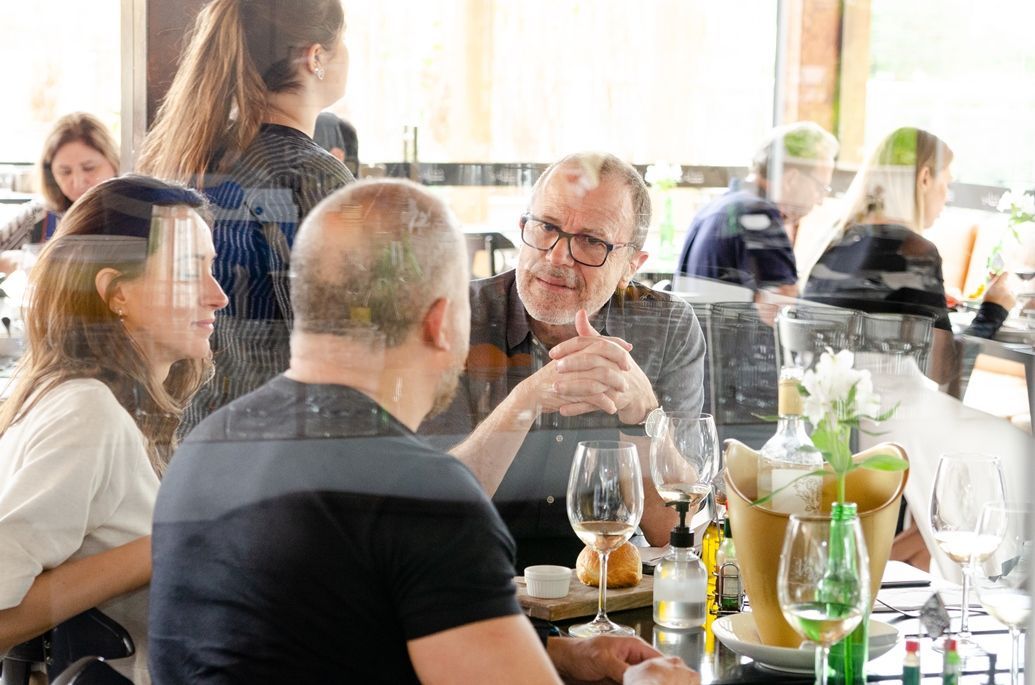 Um grupo de pessoas está sentado à mesa de um restaurante conversando entre si.