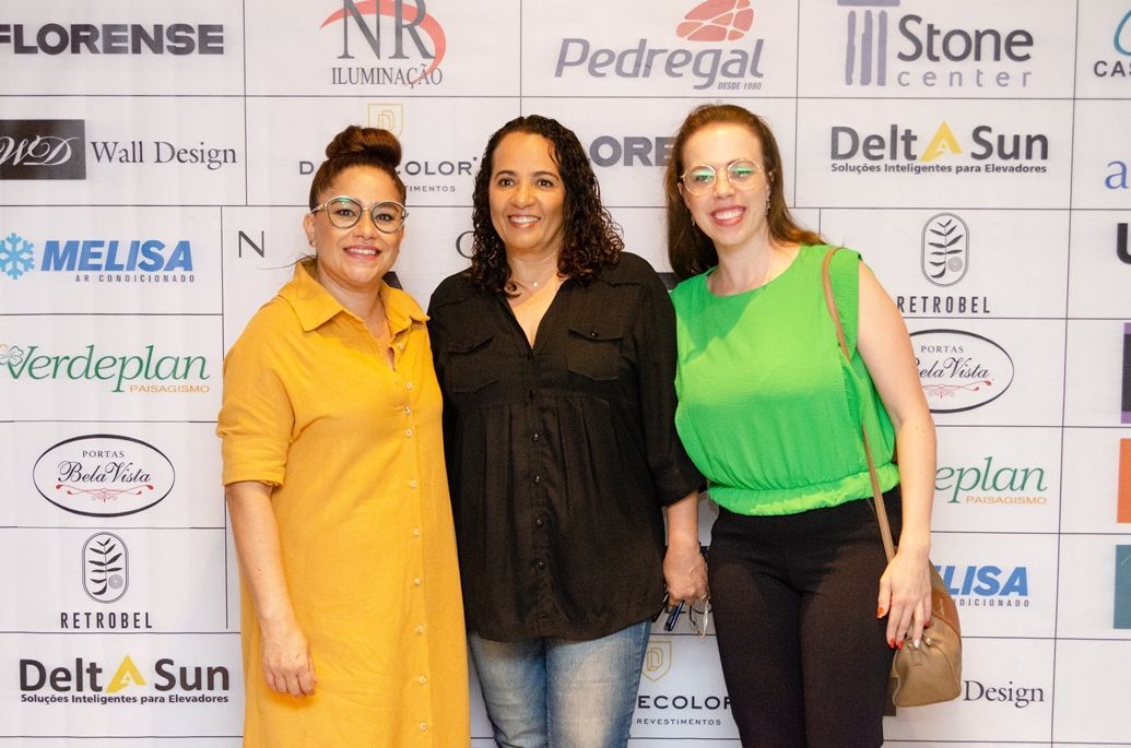 Três mulheres estão posando para uma foto em frente a uma parede com logotipos.
