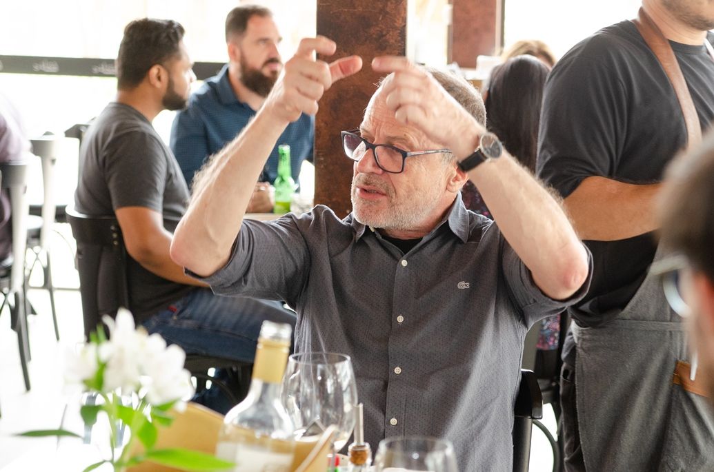 Um homem está sentado à mesa de um restaurante com as mãos no ar.