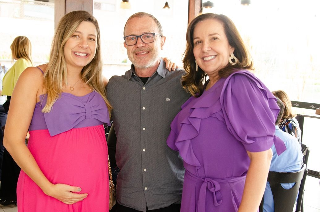 Um homem, uma mulher grávida e uma mulher de vestido roxo estão posando para uma foto.
