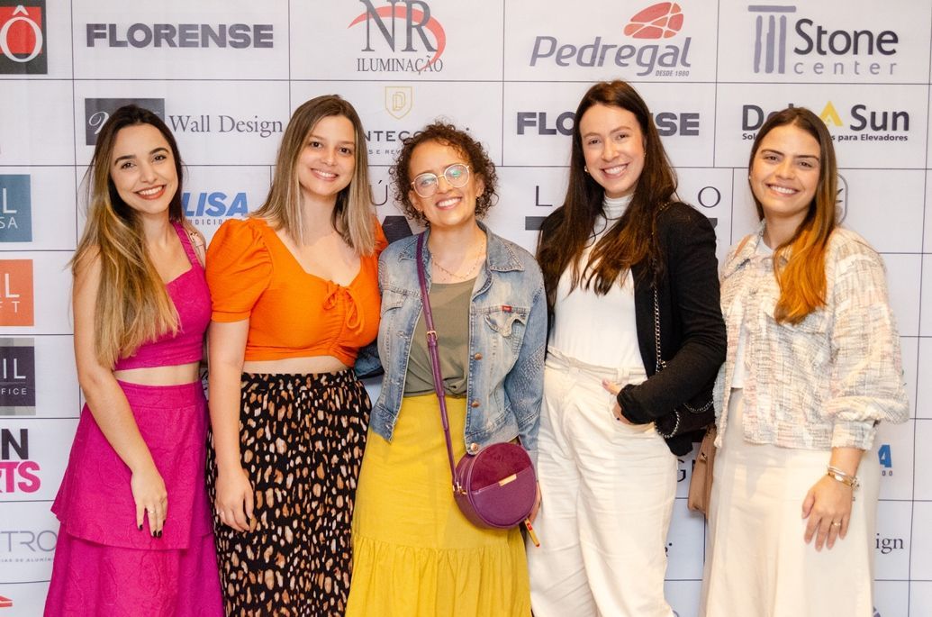 Um grupo de mulheres está posando para uma foto em frente a uma parede com logotipos.