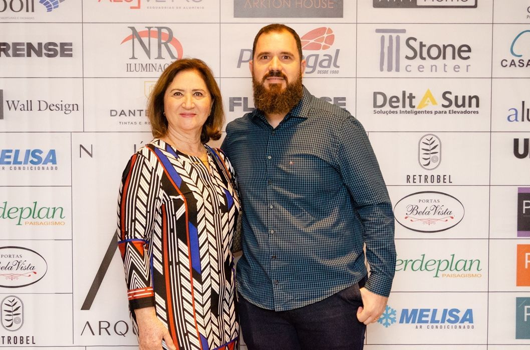 Um homem e uma mulher estão posando para uma foto em frente a uma parede com logotipos.