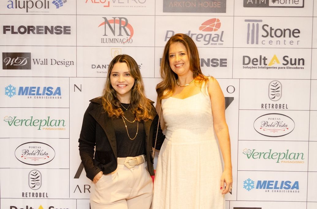 Duas mulheres estão posando para uma foto em frente a uma parede com logotipos.