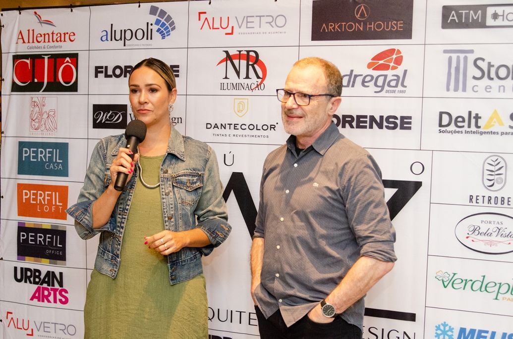 Um homem e uma mulher estão parados em frente a uma parede com logotipos