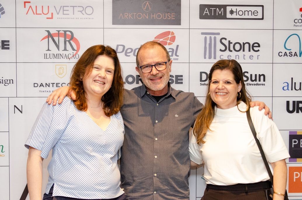 Um homem e duas mulheres estão posando para uma foto em frente a uma parede com logotipos.