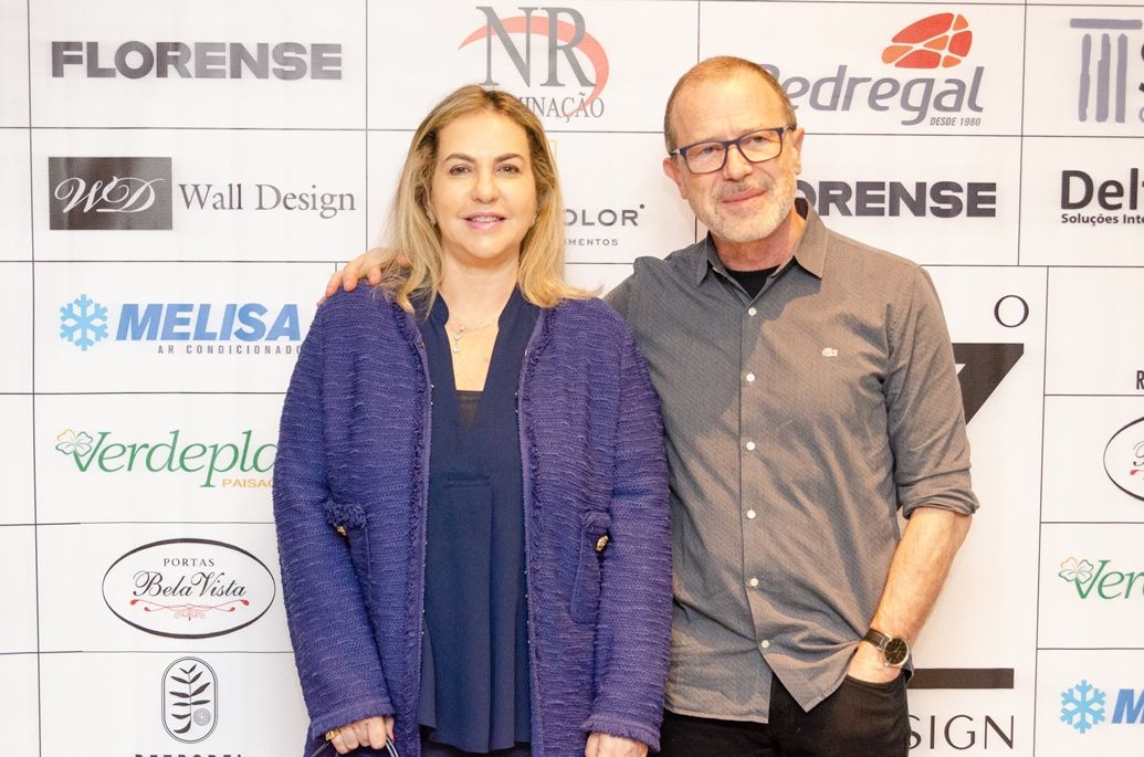 Um homem e uma mulher posam para uma foto em frente a uma parede com os logotipos do florense e do melisa