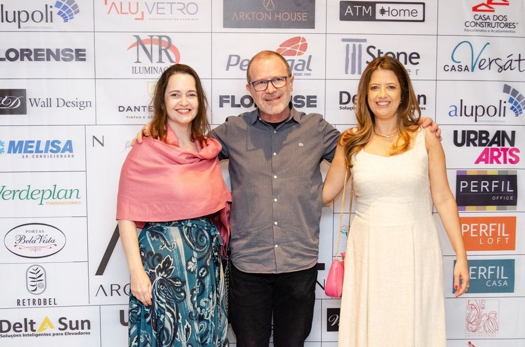 Um homem e duas mulheres estão posando para uma foto em frente a uma parede com logotipos.