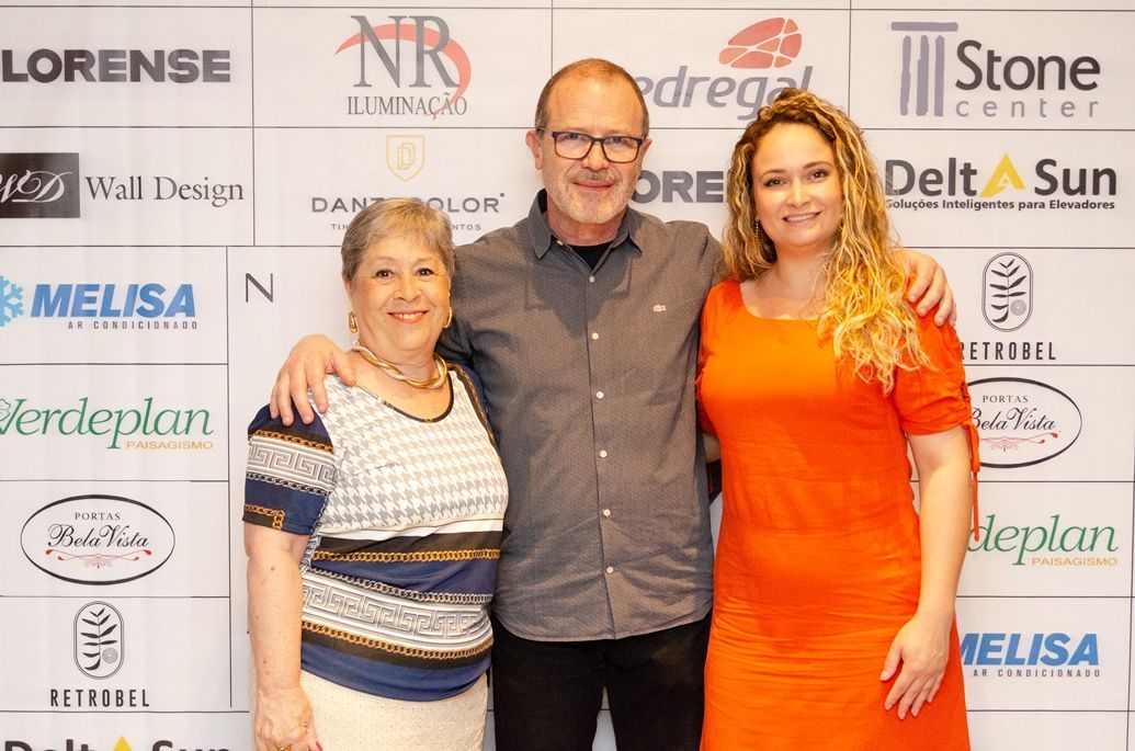 Um homem e duas mulheres estão posando para uma foto em frente a uma parede com logotipos.
