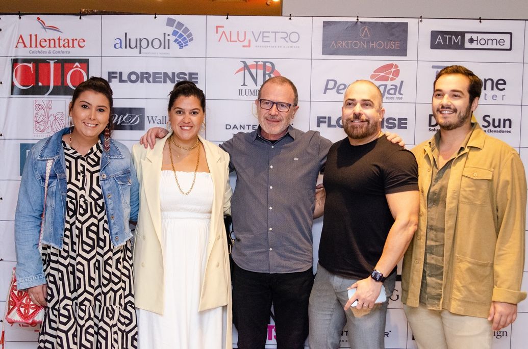Um grupo de pessoas está posando para uma foto em frente a uma parede com anúncios.
