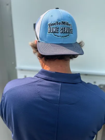 Person in a blue baseball cap and navy shirt seen from behind, standing indoors facing a wall.