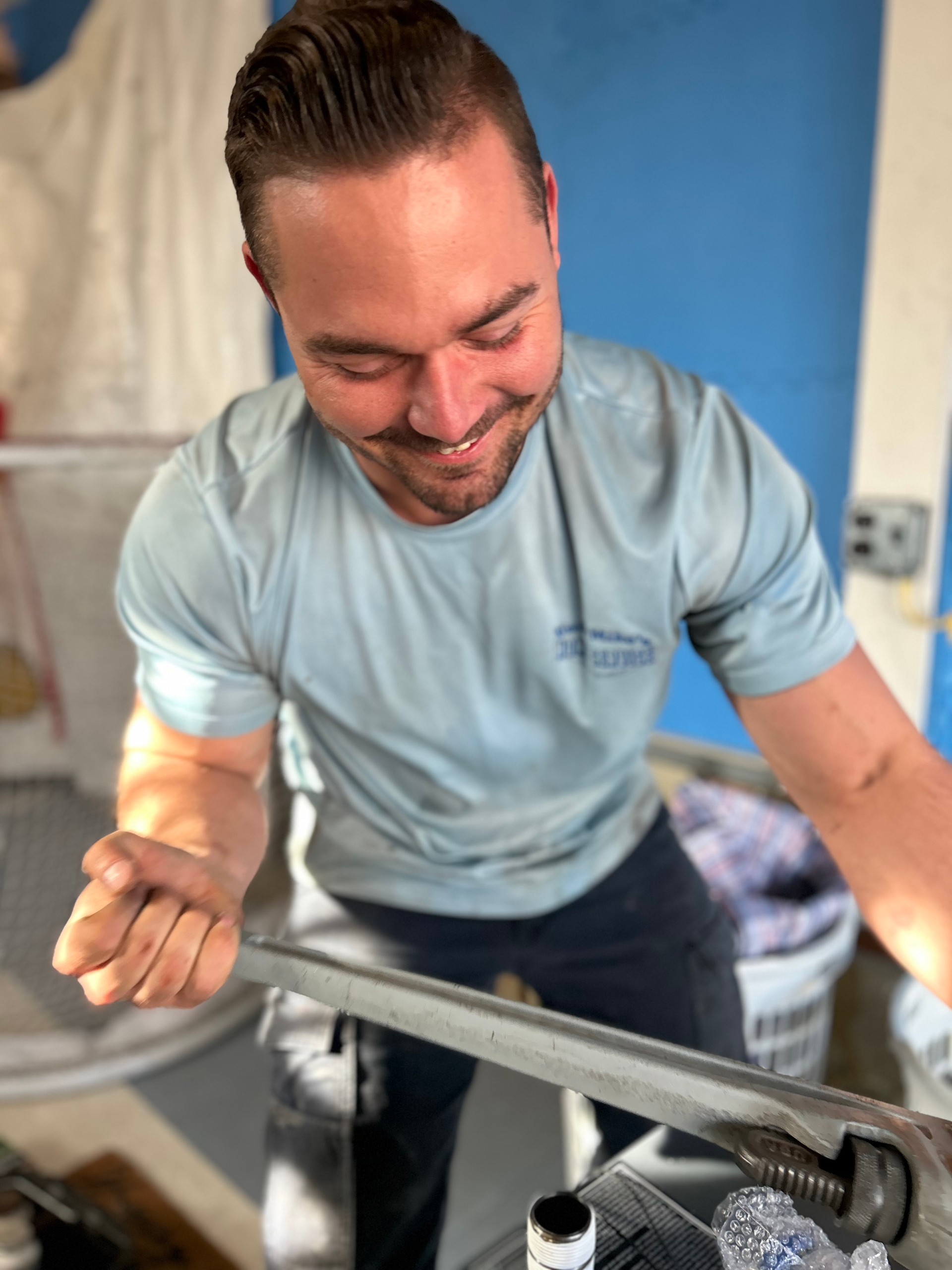 Man smiling while gripping a wrench and working on a metal pipe indoors