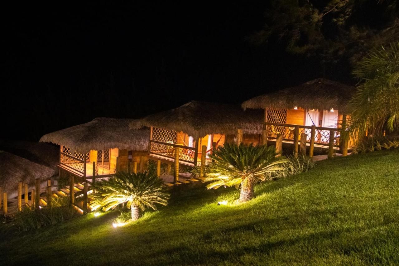 Bangalôs iluminados com telhados de palha em uma encosta gramada à noite.