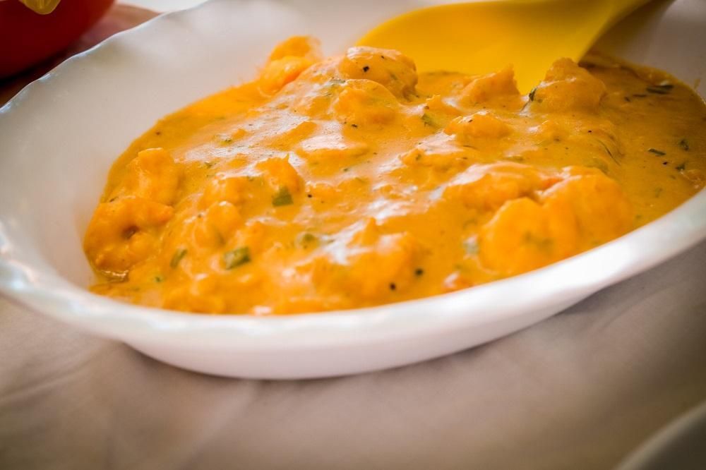 Uma tigela branca cheia de curry cremoso de camarão com molho laranja e uma colher amarela para servir.