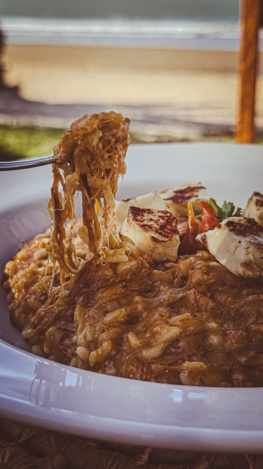 Risoto cremoso ou mingau de aveia em uma tigela branca, com uma colher para levantar uma porção e ervas por cima.