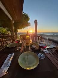 Jantar ao pôr do sol em uma mesa em um pátio à beira-mar com vista para o oceano e luzes aconchegantes.