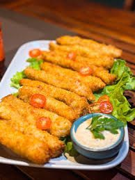 Aperitivos empanados e fritos servidos em um prato com tomates-cereja, folhas verdes e molho para mergulhar.