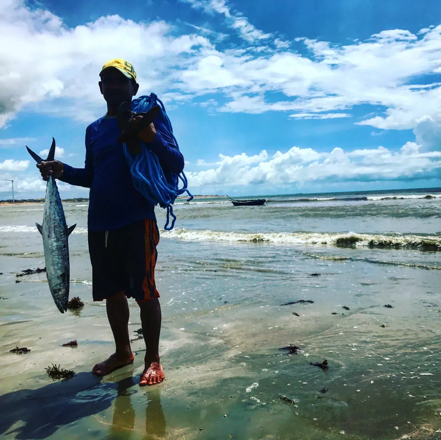 Um homem está parado na praia segurando um peixe grande