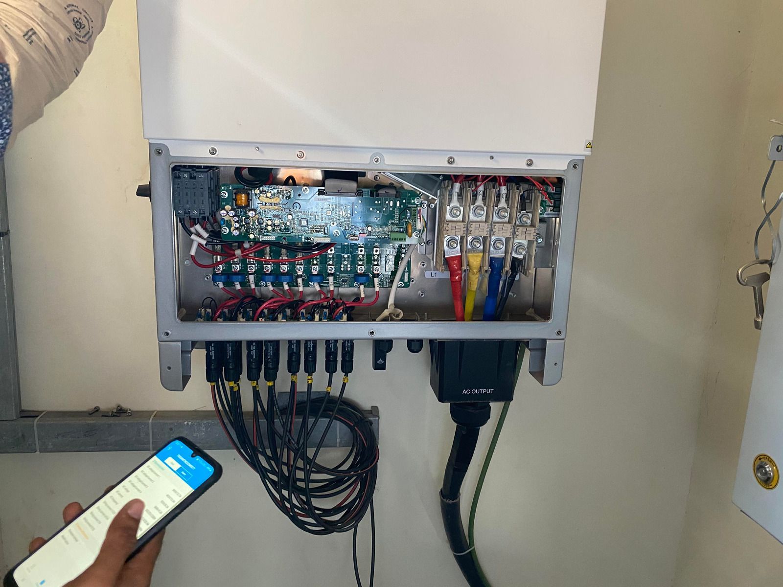 A person using a phone to check an open electrical panel with wires.
