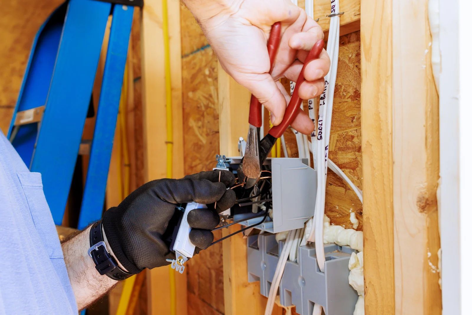 Gloved hands wiring an electrical outlet inside unfinished wooden wall framing