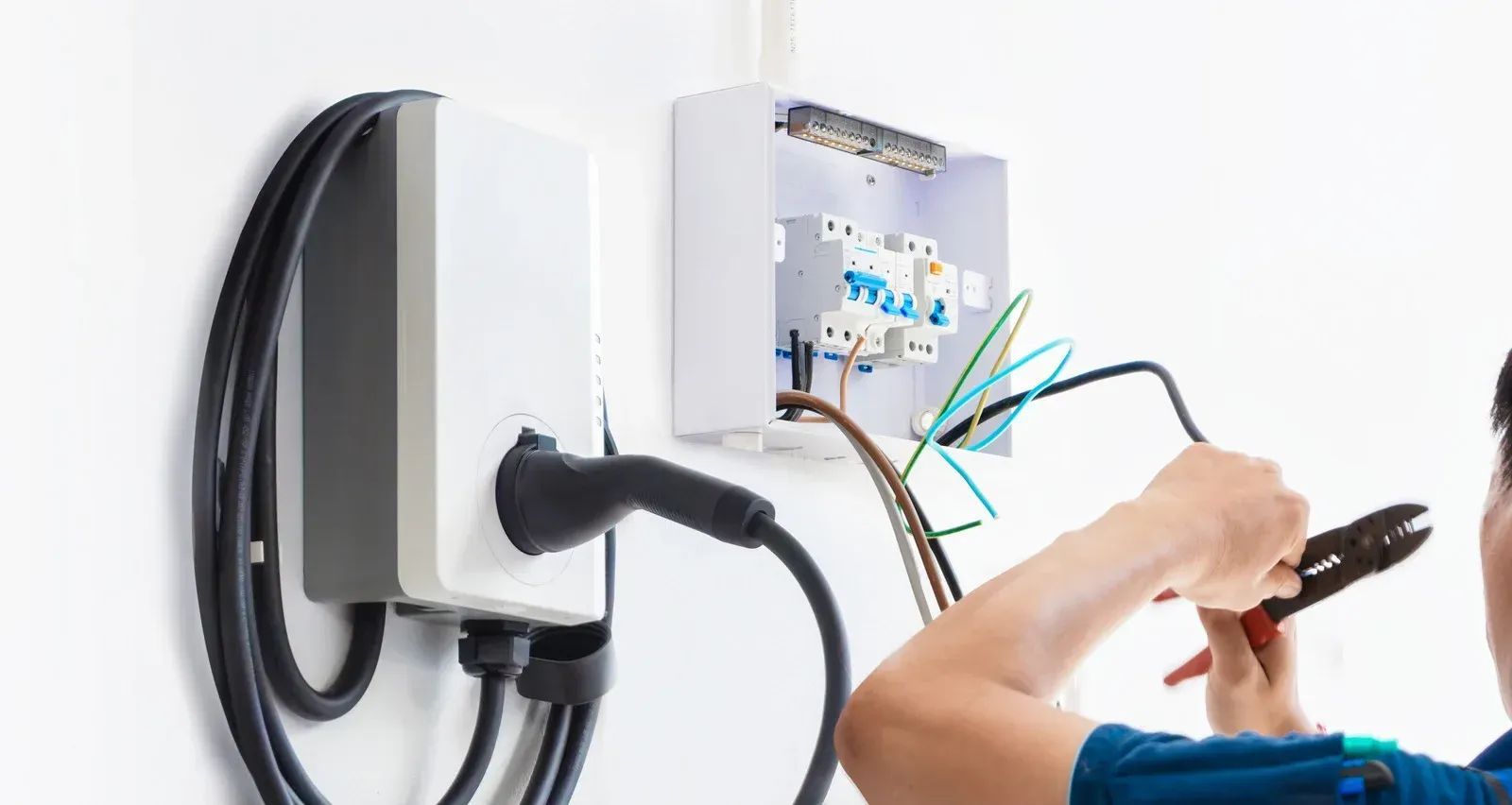 Electrician wiring a wall-mounted EV charger beside a coiled charging cable
