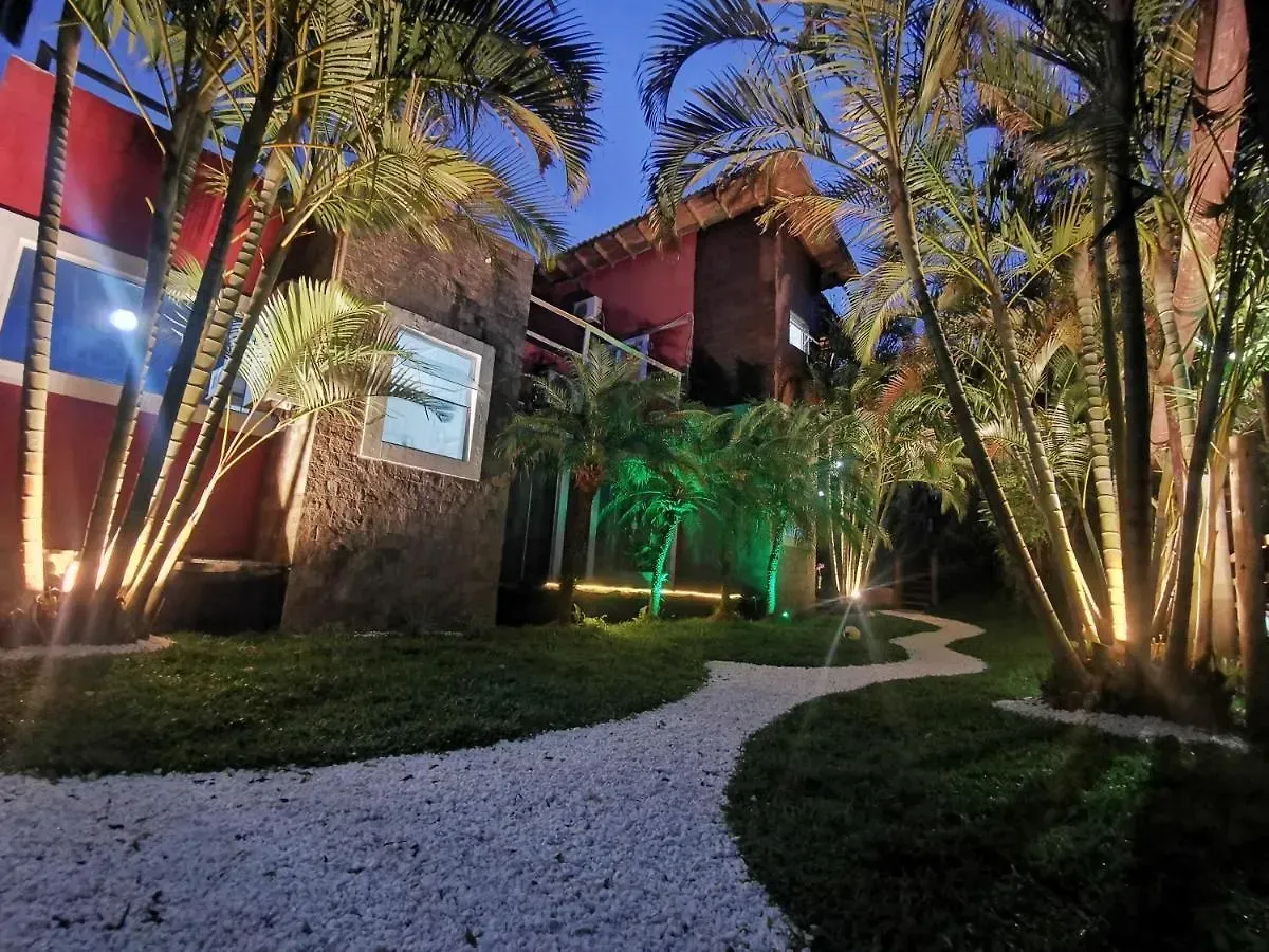 Passarela iluminada em um jardim tropical à noite, com palmeiras e um prédio aconchegantemente iluminado.