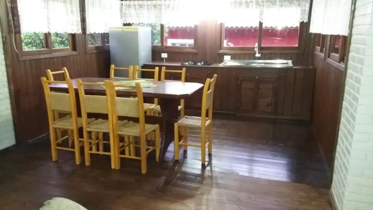 Mesa de jantar de madeira com cadeiras amarelas em uma sala com painéis de madeira, perto de janelas e com piso escuro.