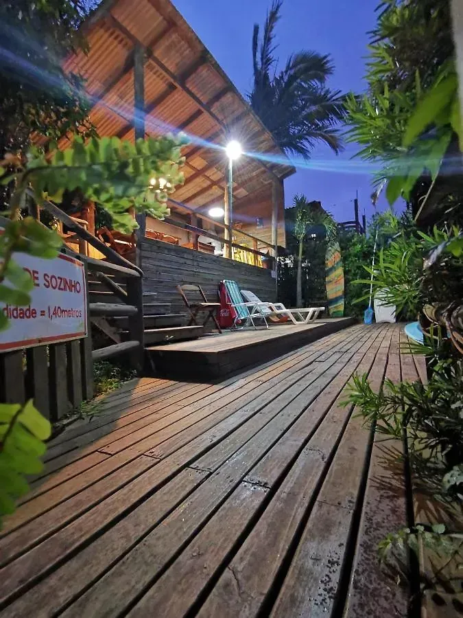 Passarela de madeira tropical ao lado de um restaurante iluminado ao entardecer, com palmeiras e vegetação exuberante.