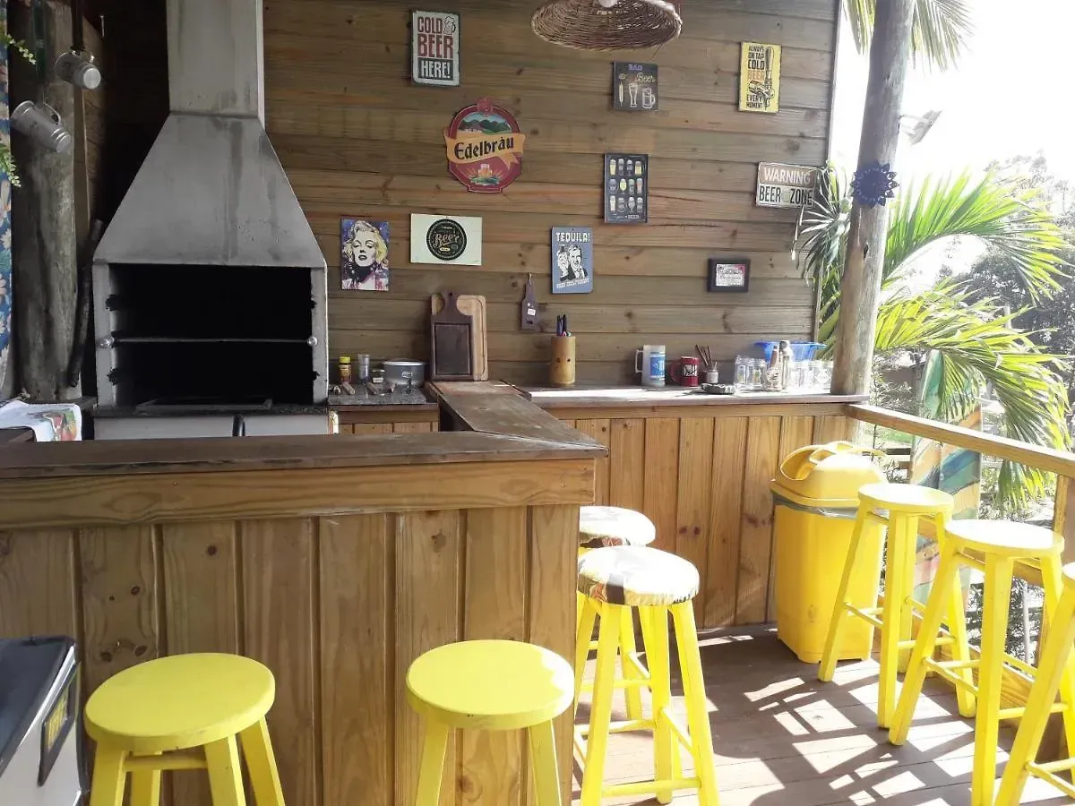 Bar de madeira ao ar livre com banquetas amarelas, churrasqueira e plantas tropicais ao longo do deck.