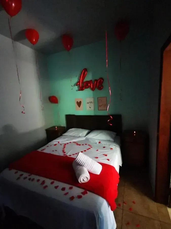 Quarto romântico com balões vermelhos, colcha com estampa de coração e decoração de parede com a palavra 