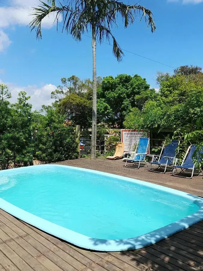 Piscina no quintal com água turquesa, deck de madeira, espreguiçadeiras e árvores tropicais sob um céu azul.