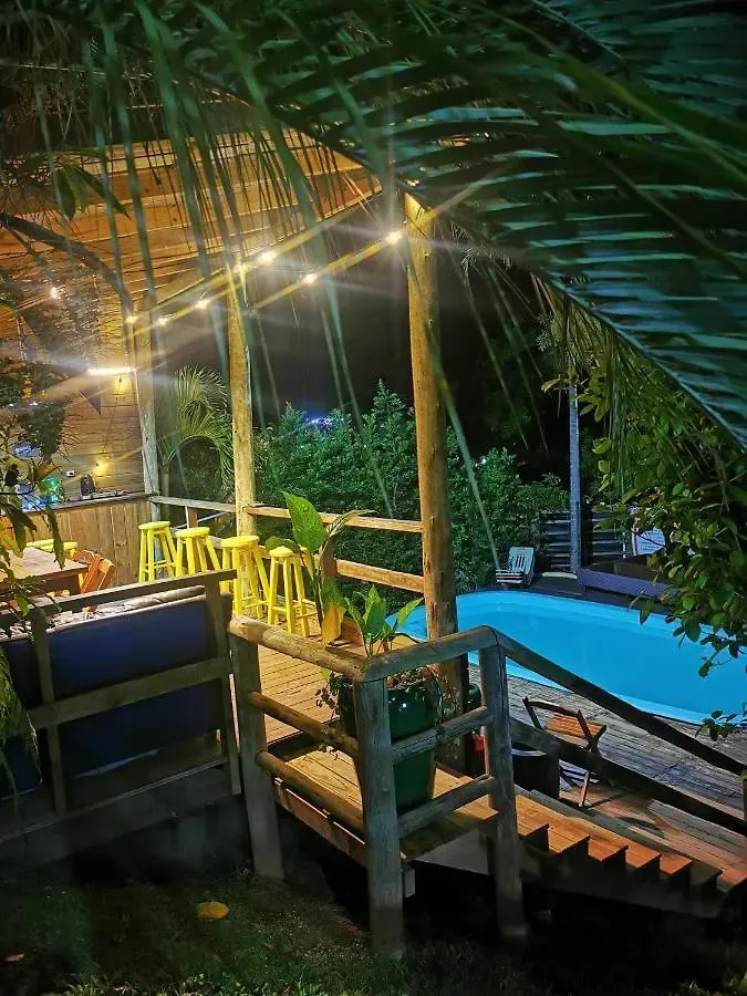 Terraço tropical com luzes de corda em tons quentes, corrimãos de madeira e uma piscina azul à noite.