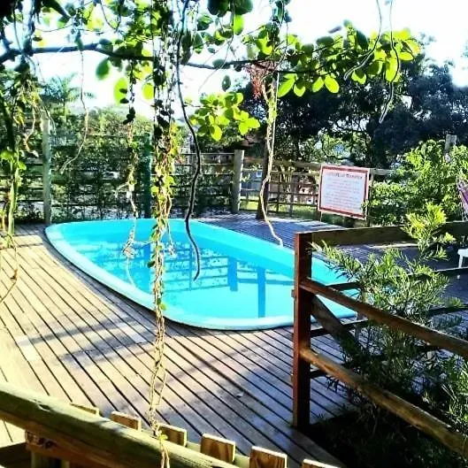 Piscina azul ao lado de um deck de madeira com corrimão, em um jardim arborizado.