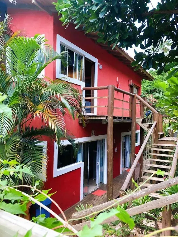 Cabana vermelha de dois andares com varanda e escadas de madeira em meio a uma exuberante vegetação tropical.