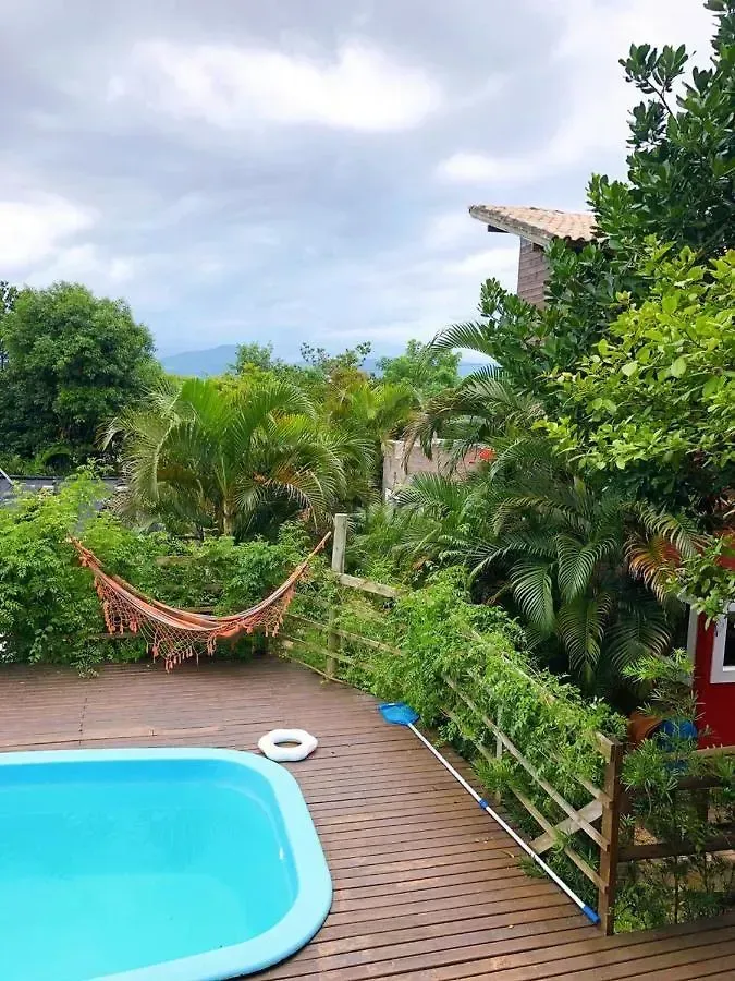 Piscina no quintal ao lado de uma rede e vegetação tropical exuberante sob um céu nublado.