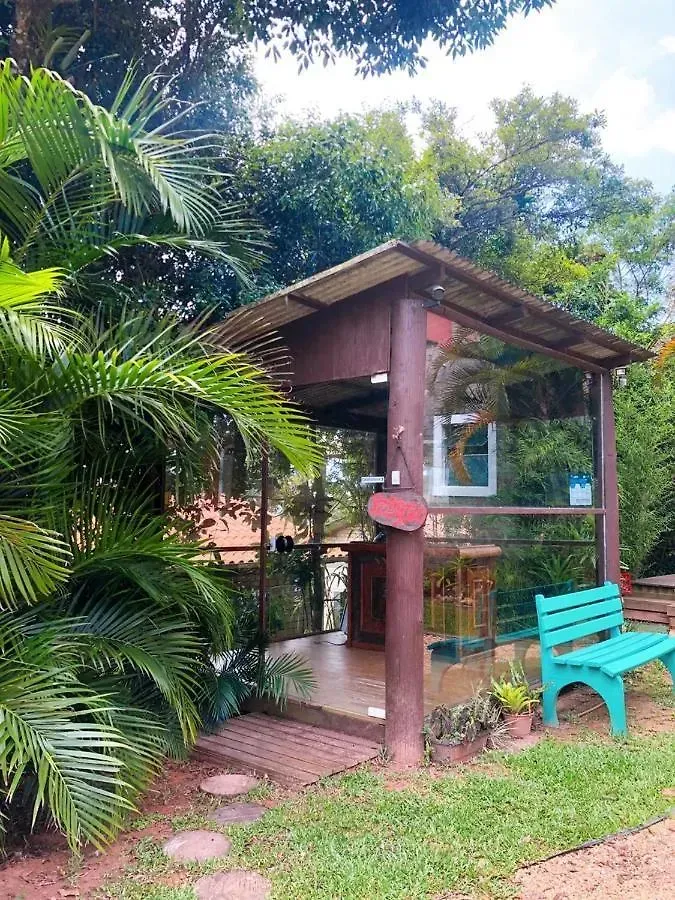 Pequena cabana de jardim tropical com um banco turquesa, rodeada por vegetação exuberante.