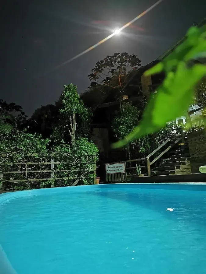 Piscina noturna com luar brilhante, vegetação exuberante e escadas ao lado de águas turquesa.