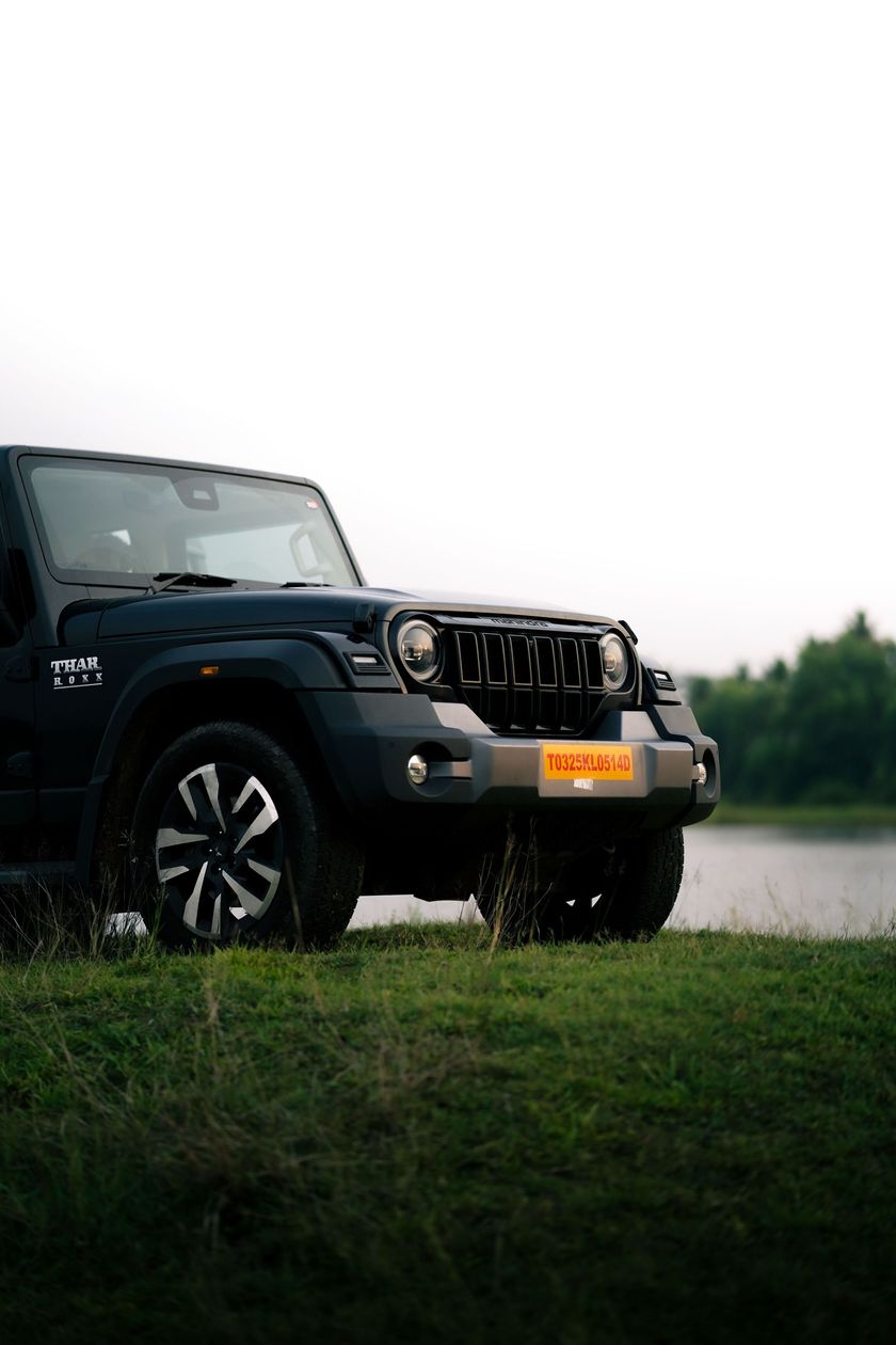 Jeep Wrangler preto estacionado na grama perto de um lago, vista frontal com placa laranja.