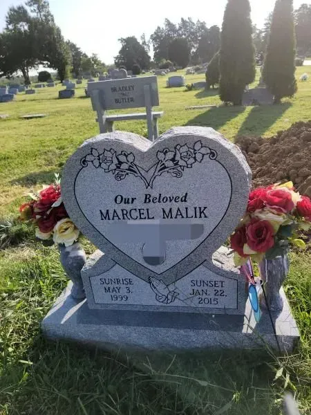 A heart shaped gravestone in a cemetery that says our beloved marcel malik