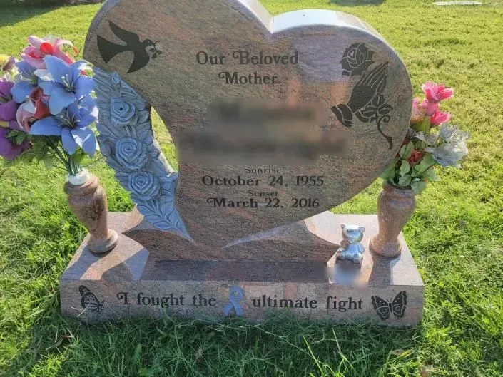 A heart shaped gravestone with flowers in vases in a cemetery.