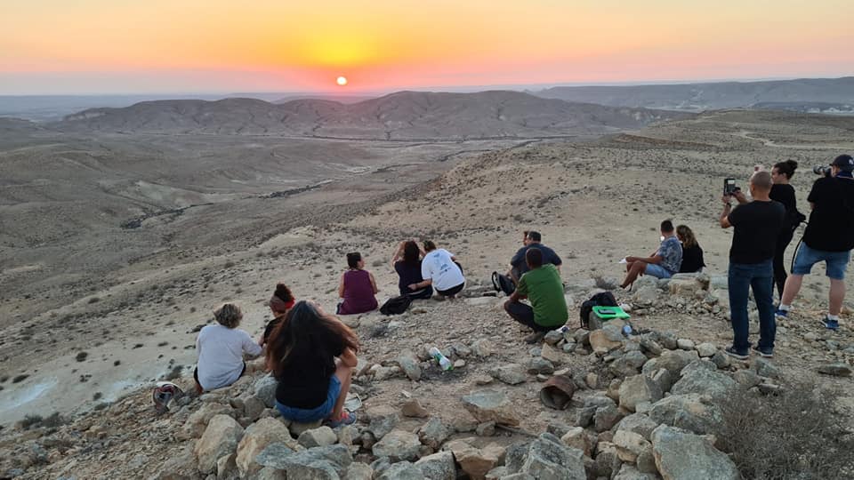 קבוצת אנשים יושבת על ראש גבעה סלעית וצופה בשקיעה.