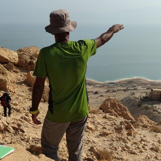 גבר בחולצה ירוקה וכובע עומד על גבעה סלעית המשקיפה על האוקיינוס