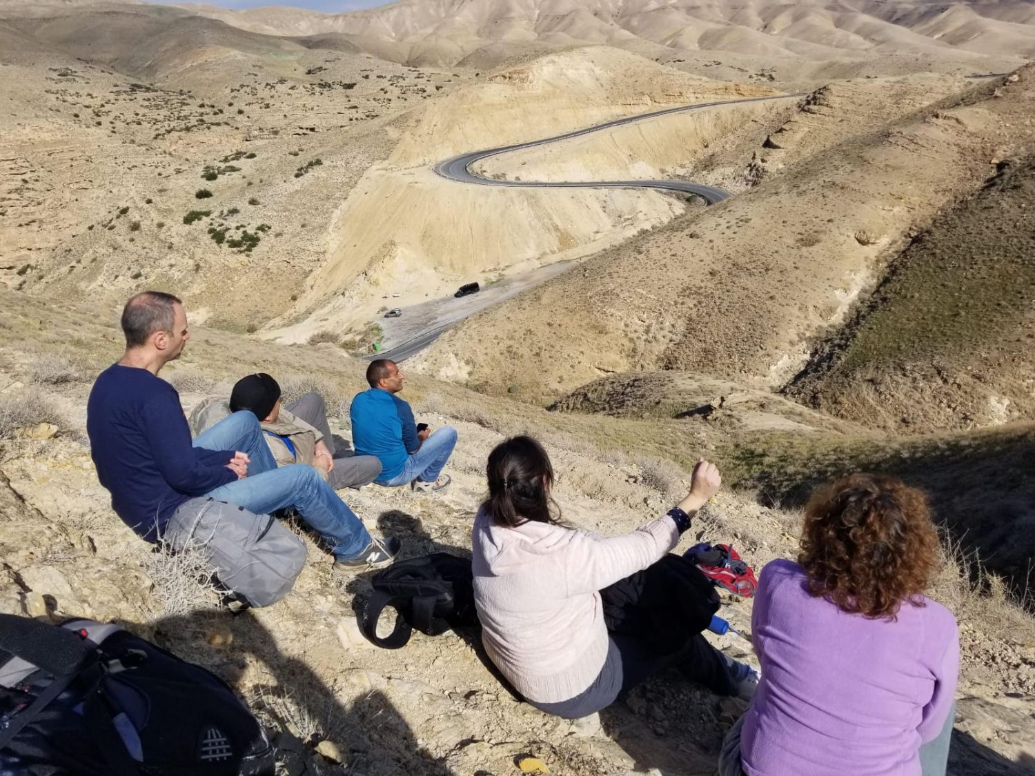 קבוצה של אנשים יושבת על ראש גבעה ומסתכלת על כביש.