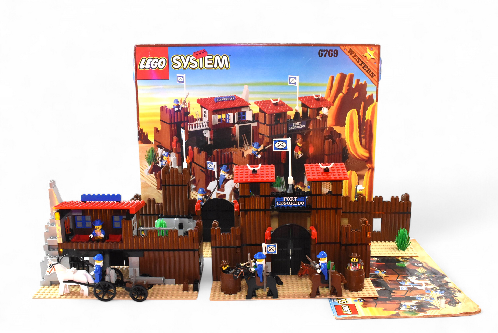 Ensemble LEGO Fort de l'Ouest avec boîte, figurines et diligence. Bâtiments marron, touches de bleu, figurines en action.