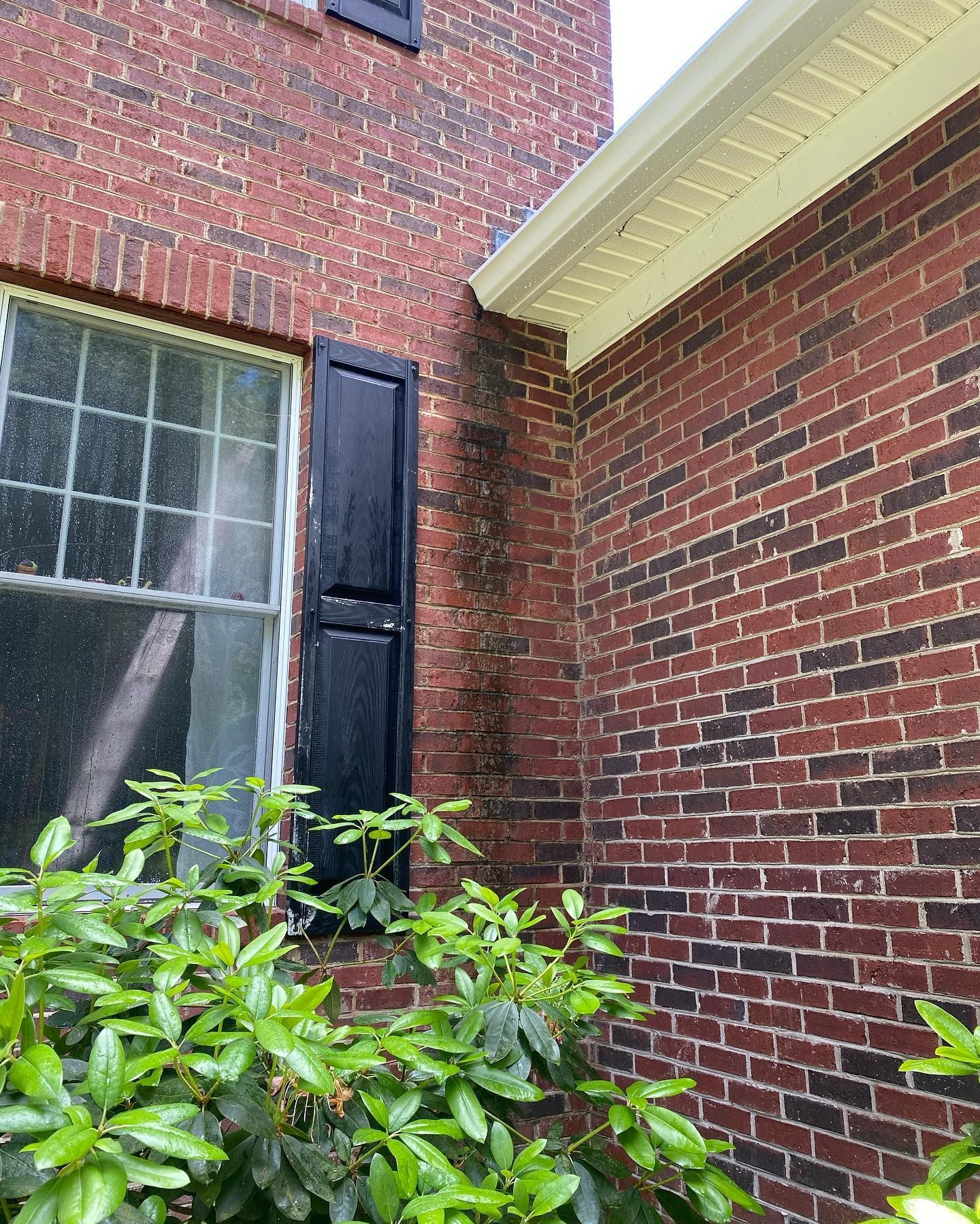 A red brick house with black shutters and a window.