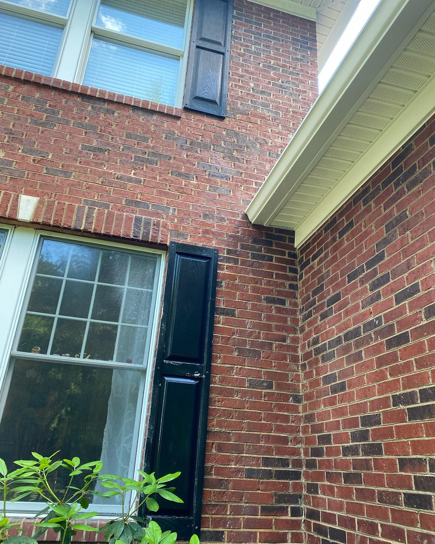 A brick building with a window and black shutters on it.