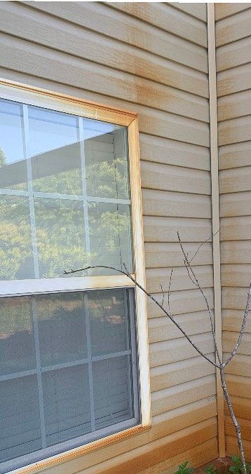 A window on the side of a house with a tree in front of it.