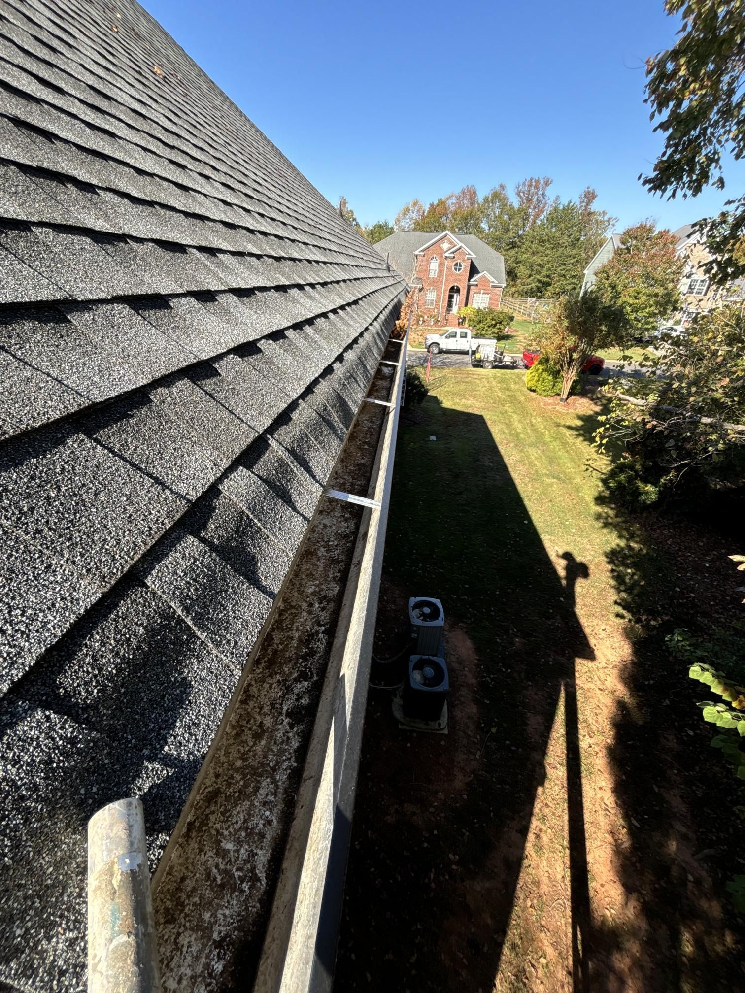 A gutter on the side of a house with a roof in the background.