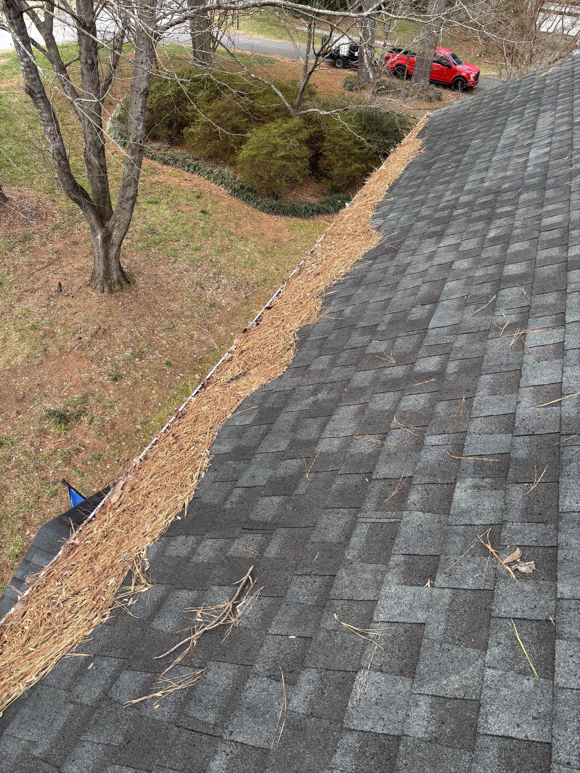 An aerial view of a roof with a gutter filled with leaves.